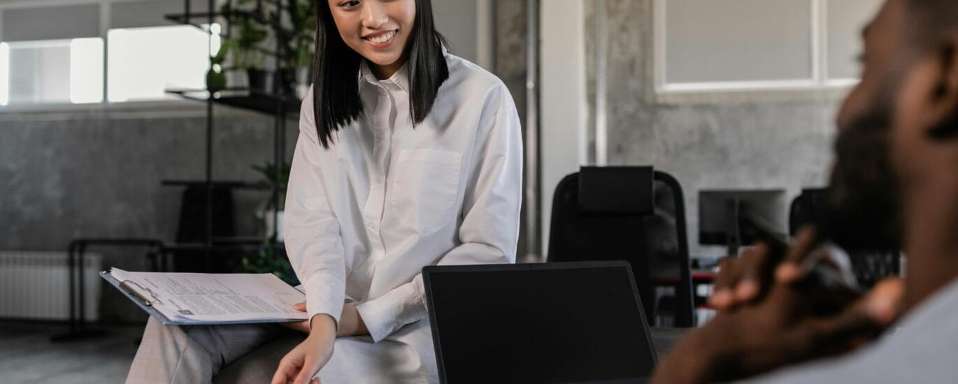 Asian woman in white long sleeves engages with a colleague in a modern workspace. Office collaboration.