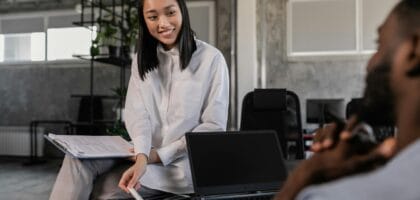 Asian woman in white long sleeves engages with a colleague in a modern workspace. Office collaboration.