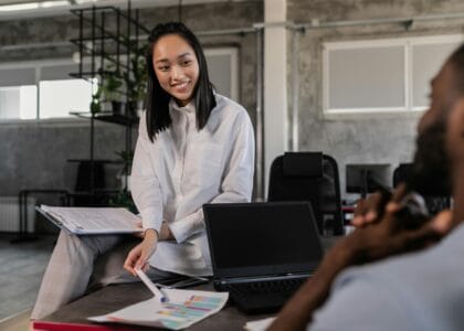 Asian woman in white long sleeves engages with a colleague in a modern workspace. Office collaboration.